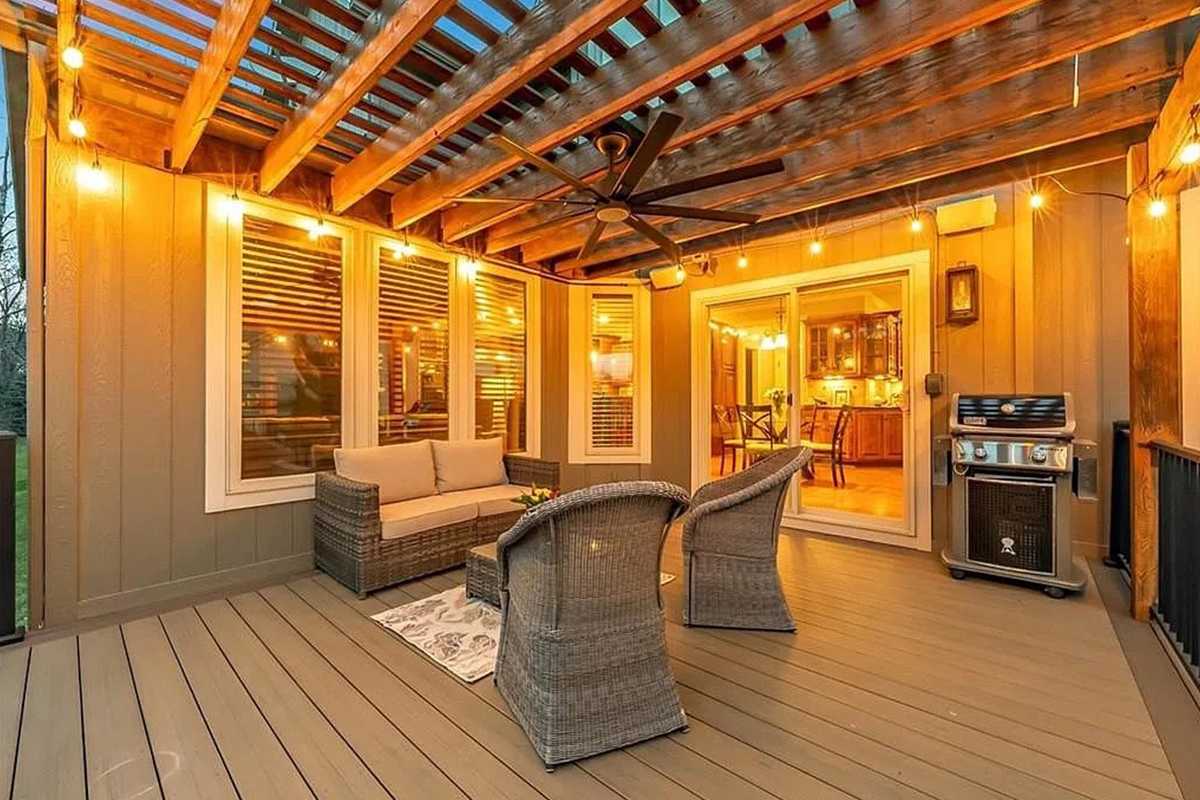 Covered porch with a ceiling fan, string lights, and wicker seating on a composite deck, with a gas grill beside the sliding door